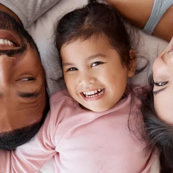 Happy family of three lying down together smiling, showing close bond and joyful moments