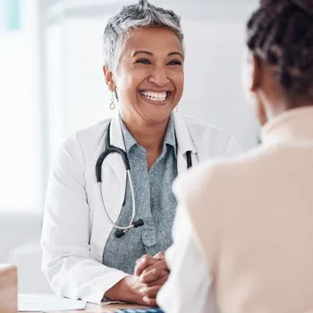 Smiling female doctor with gray hair and stethoscope talking to patient in a bright medical office.