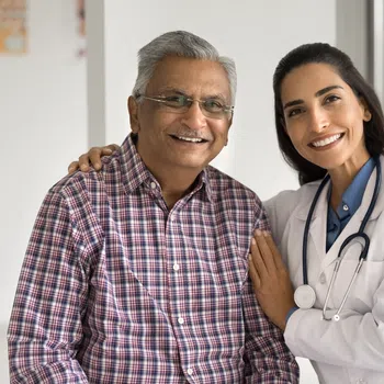 Smiling female doctor with stethoscope embraces senior male patient in medical office with skeleton model.