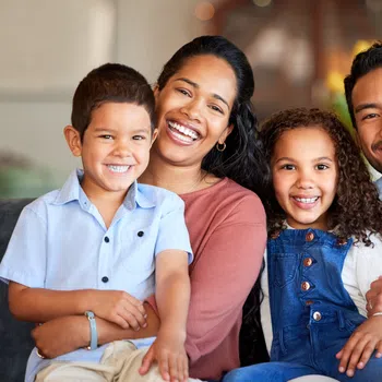 Smiling happy family of four sitting closely together on a couch indoors, showing warmth and love