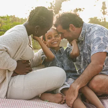 Happy diverse family enjoying a picnic outdoors on a blanket with loving parents and smiling child.