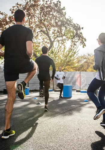 Group of people exercising outdoors performing high knees in fitness training session on sunny day