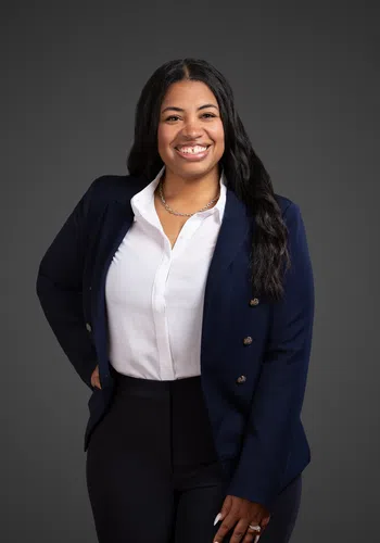 Confident woman in a navy blazer and white blouse smiling against a dark background