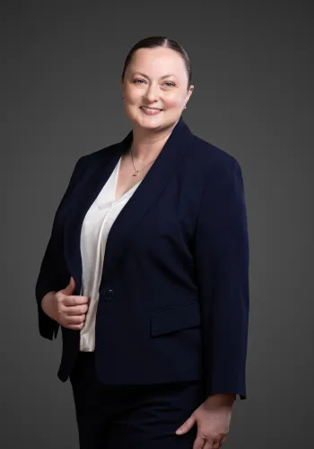 Confident woman in navy blazer and white blouse smiling against a gray studio background.