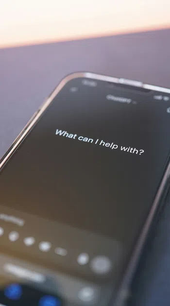 Smartphone screen displaying digital assistant prompt 'What can I help with?' in low light.