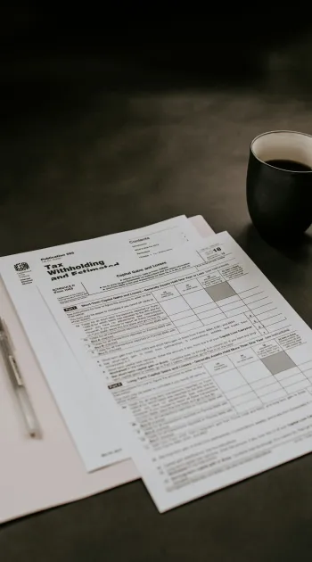 Tax forms and documents next to a pen and black coffee cup on a dark surface.
