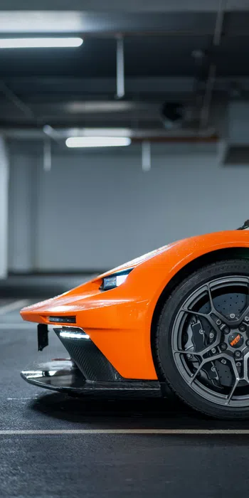 Close-up of an orange sports car front wheel and headlight in a dimly lit parking garage.