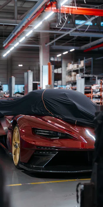 Red high-performance sports car with gold wheels partially covered by black cloth in a workshop.