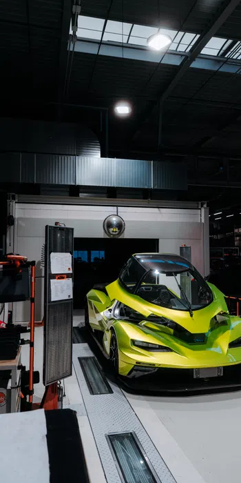 Bright yellow futuristic race car parked inside a dimly lit industrial workshop or garage.