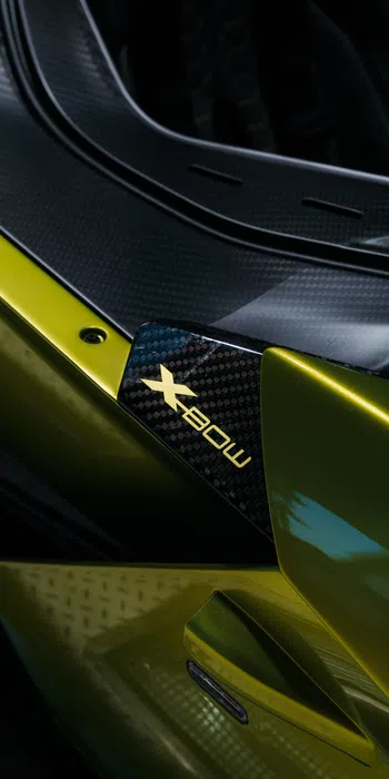 Close-up of a green sports car with carbon fiber detail featuring an X-Bow logo.