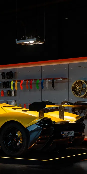 Yellow high-performance sports car in showroom with wheels and color samples displayed on wall behind it.