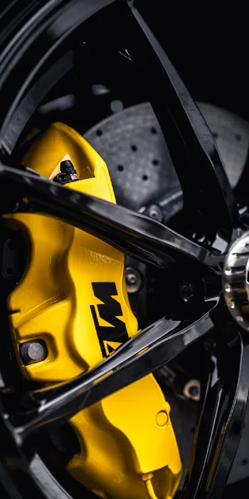 Close-up of black car wheel with yellow brake caliper and drilled brake rotor, highlighting performance components.
