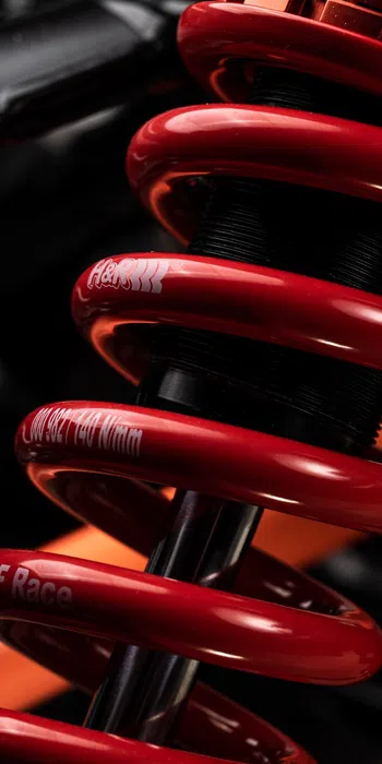 Close-up of a red coil spring shock absorber in a vehicle suspension system with detailed mechanical components.