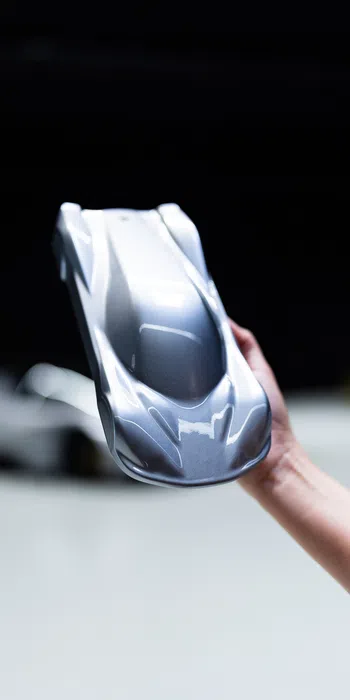 Hand holding sleek silver futuristic sports car model against dark background.