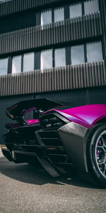 Close-up of a purple sports car rear with carbon fiber details and sleek design parked by a modern building.
