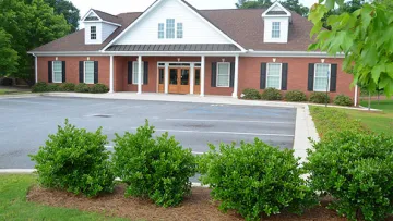 A modern brick building with a manicured lawn and parking area, surrounded by greenery.