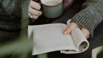 a person holding a book and a cup of coffee