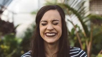 a woman smiling in front of a greenhouse