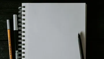 An empty sketchbook with pens and markers on a black wooden surface.