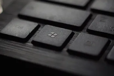 Close-up of a black keyboard with a Windows logo key in focus on a wooden surface.