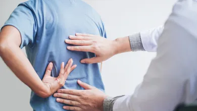 Doctor examining a patient's lower back pain by palpating the spine area in a clinical setting.