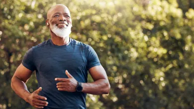 Smiling mature man jogging outdoors in blue shirt with greenery background and smartwatch on wrist