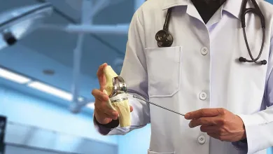 Doctor in white coat with stethoscope holding and pointing to a knee joint model in clinical setting