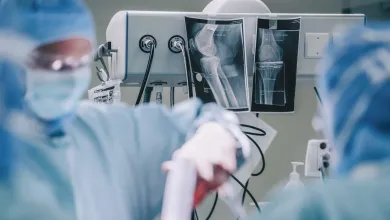 Surgeons in operating room with bone X-rays displayed on medical equipment during surgery.