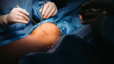 Surgeons performing a knee surgery with instruments focusing on the knee joint under bright lighting.