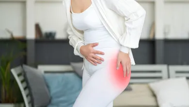 Woman in white outfit holding hip in pain, highlighted red area indicating hip discomfort or injury.