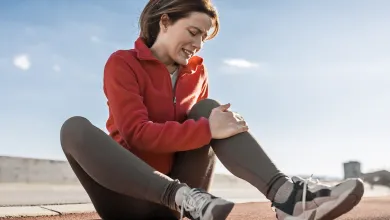 Woman sitting on track holding her injured knee in pain during outdoor exercise session