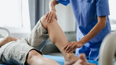 Physical therapist in blue scrubs assisting patient with leg stretch during rehabilitation session.