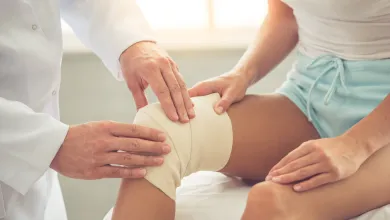 male doctor examining female patient's bandaged knee