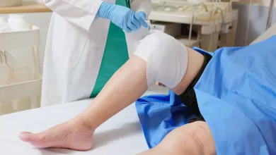 Medical professional adjusts knee bandage on patient lying down in clinical setting with blue drape.