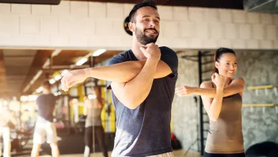 Man and woman stretching arms before workout in bright gym with mirrors and equipment