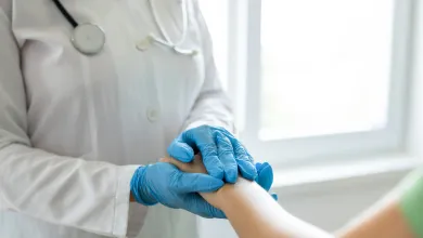 Doctor wearing gloves holding patient's hand gently during a medical consultation in bright clinic.