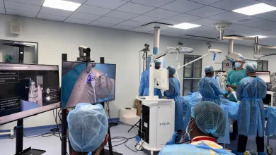 Medical team performing robotic-assisted surgery in operating room with monitors displaying procedure details.