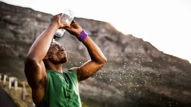 Man in green sleeveless shirt splashes water on his face outdoors near rocky mountains during sunset.