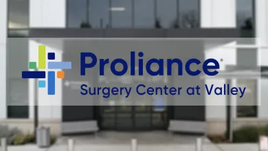 Proliance Surgery Center at Valley logo with colorful cross symbol over blurred medical building entrance.
