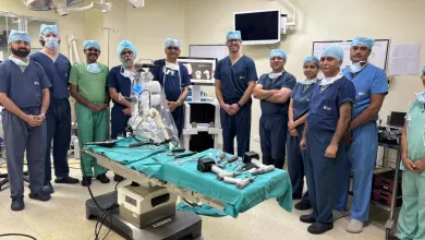 Medical team in surgical scrubs standing around an operating table with surgical tools in a hospital room.