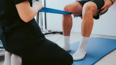 Physical therapist assists patient with knee resistance band exercises on blue mat indoors