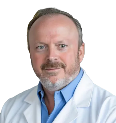 Portrait of a male doctor with beard, wearing a white coat and blue shirt, smiling gently.