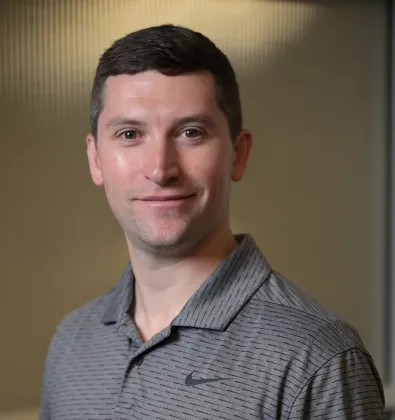 Smiling man wearing a gray Nike polo shirt against a blurred indoor background.