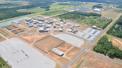 Aerial view of a large training facility with multiple buildings, open fields, and adjacent wooded areas under clear sky