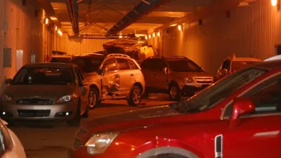 Damaged and parked cars inside a dimly lit underground garage with orange lighting and metal walls.