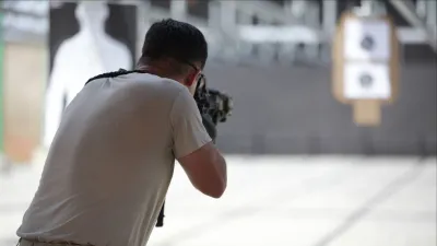 Man aiming a rifle at shooting range target wearing a gray t-shirt in an indoor shooting range.