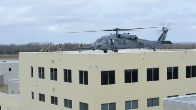 Military helicopter landing on a building rooftop with soldiers disembarking during a training exercise.