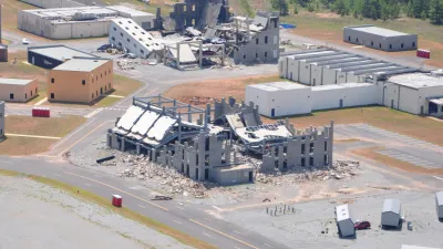 Aerial view of partially demolished buildings in an industrial area with surrounding roads and greenery.