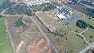 Aerial view of a winding test track next to a large building surrounded by greenery and roads.