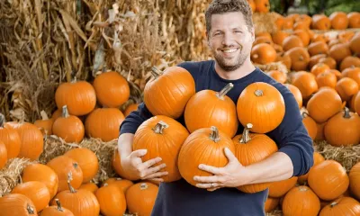 a person standing next to a pile of pumpkins